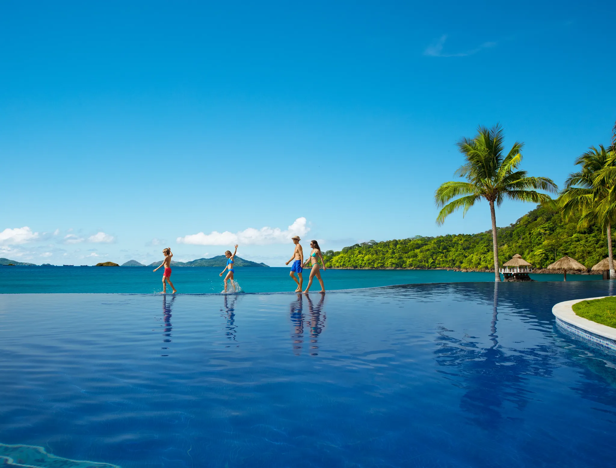 Family walking and playing in the infinity pool overlooking the ocean at Dreams Playa Bonita Panama, surrounded by lush tropical scenery.