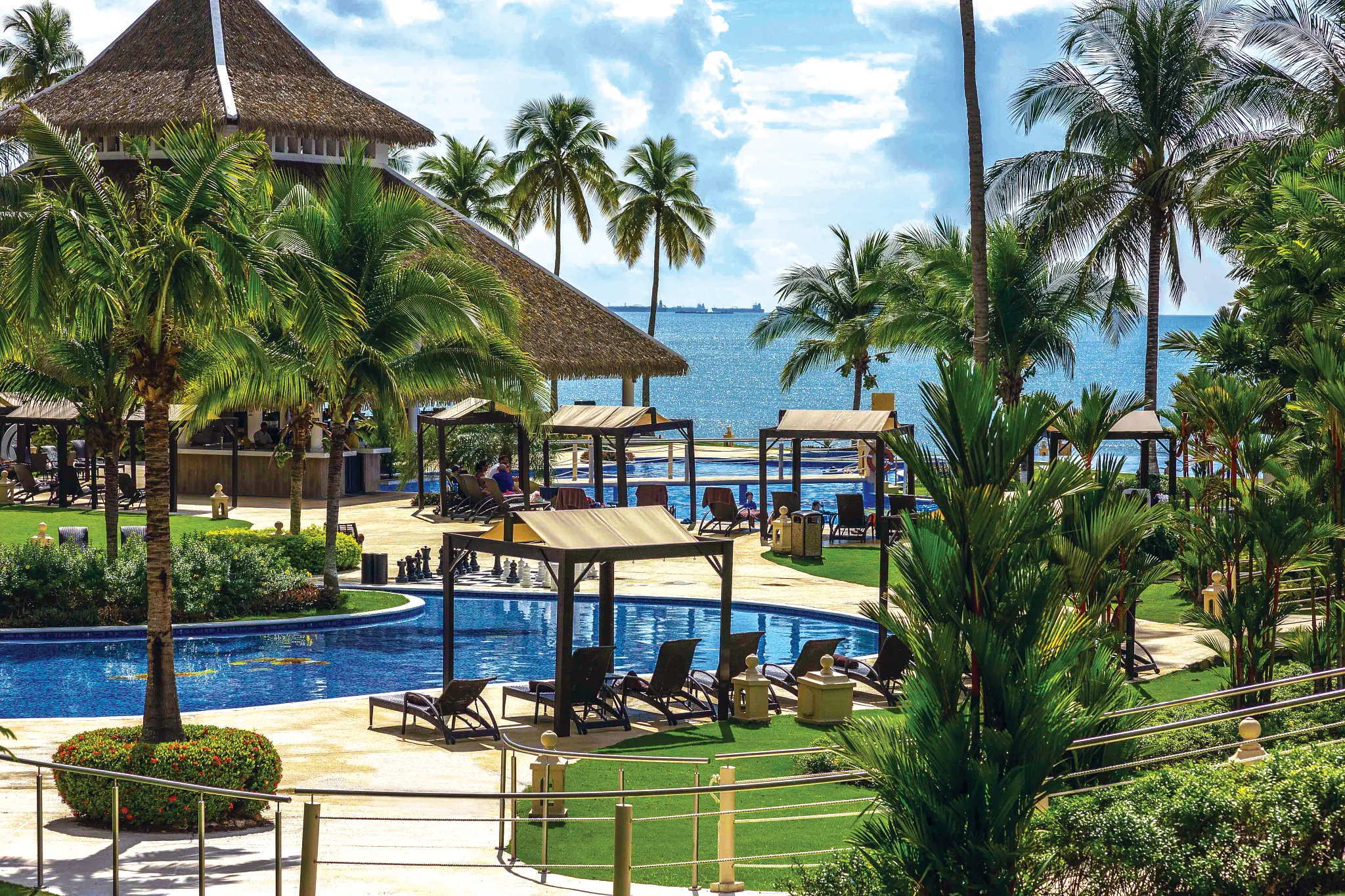 Oceanfront pool area with palm trees and shaded cabanas at Dreams Playa Bonita Panama, offering relaxing views of the Pacific Ocean.