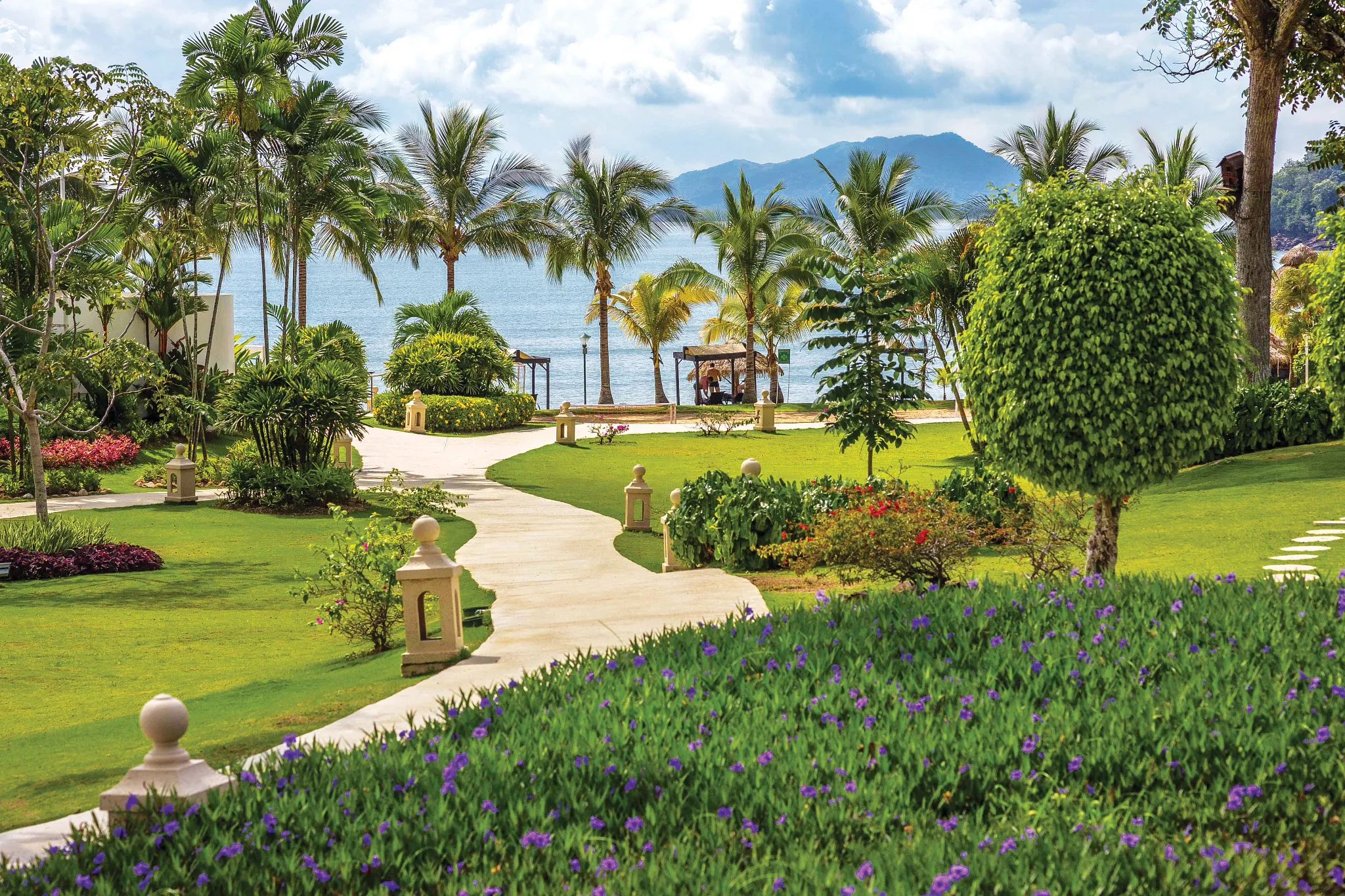 Tropical garden pathways leading to the beach at Dreams Playa Bonita Panama, surrounded by palm trees, ocean views, and lush greenery.